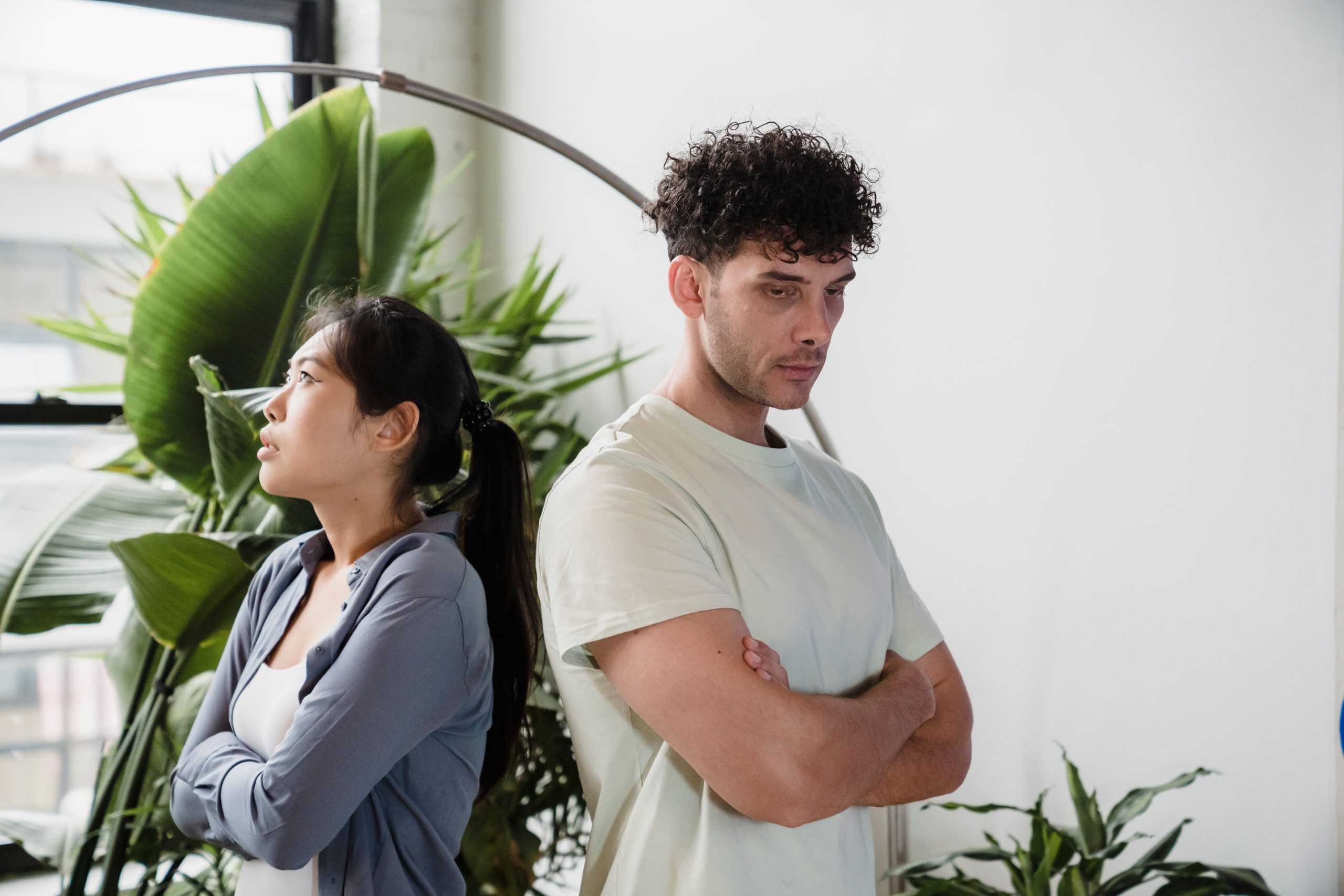 Jeune couple dos à dos, contrariés parmi plantes vertes